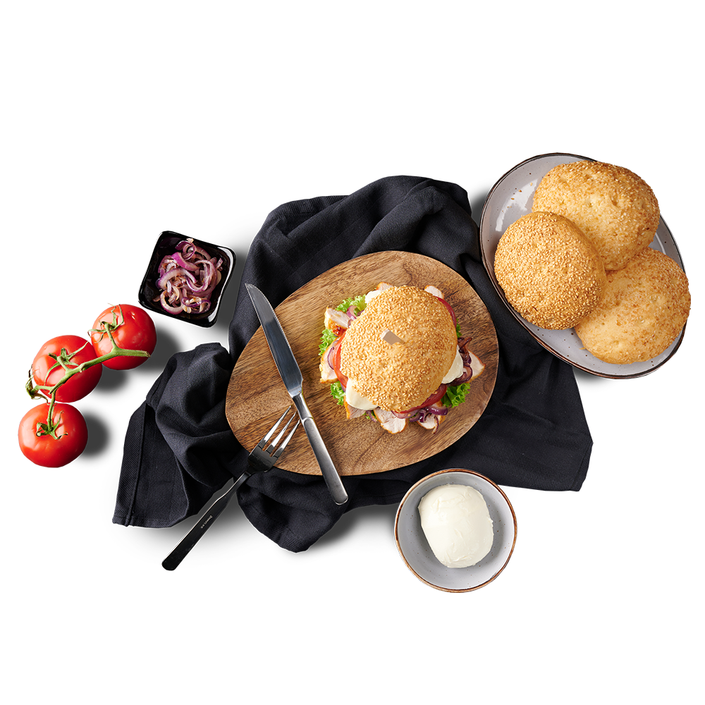 Hähnchenbrustbrötchen von oben: Drei Brötchen auf Teller, daneben mit Hähnchenbrust und Salat belegtes Brötchen auf Holzbrett auf schwarzem Tuch, Besteck, eine Rispe Tomaten, ein Schälchen Salz, ein Schälchen Zwiebeln